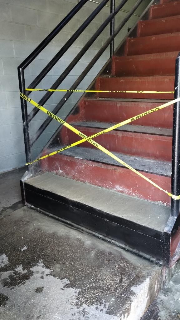 Repaired lower concrete step with black metal edge and caution tape