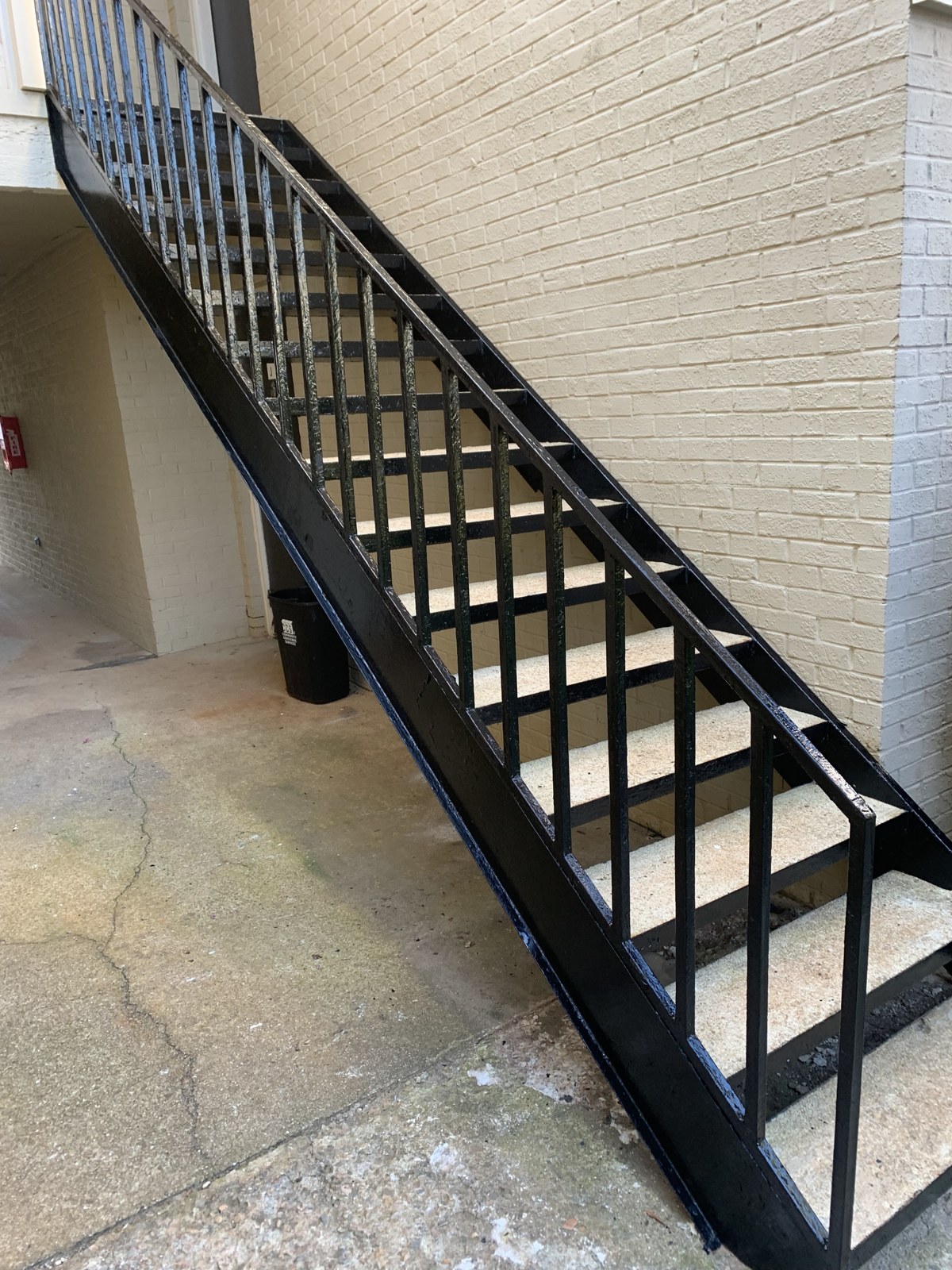 Black exterior steel staircase with matching metal railings beside a brick building